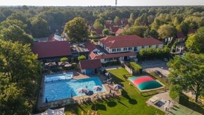 Vue aérienne d’un quartier résidentiel avec une piscine, un court de tennis et des maisons aux toits rouges.