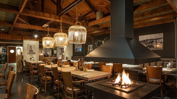 Un restaurant au décor intérieur en bois, doté de luminaires suspendus et d’un foyer central.