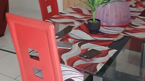 Un coin repas avec une table en verre, des chaises rouges et une porte en bois en arrière-plan.