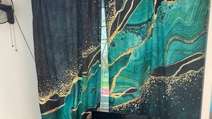 Une pièce avec un rideau noir et turquoise à motifs, un meuble TV noir et une petite table blanche.