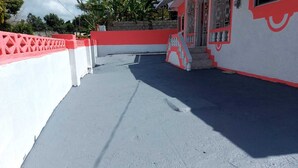 Un toit-terrasse aux couleurs rouge et blanche, un escalier menant à une porte et un ciel dégagé.