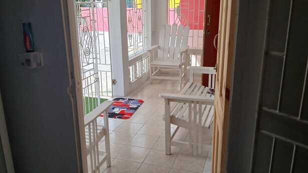 Un couloir avec des chaises blanches, un tapis coloré et une porte donnant sur l’extérieur.