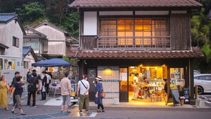 En traditionell japansk byggnad med ett tak täckt av tegelpannor och en träfasad, omgiven av fotgängare och en parkerad bil.