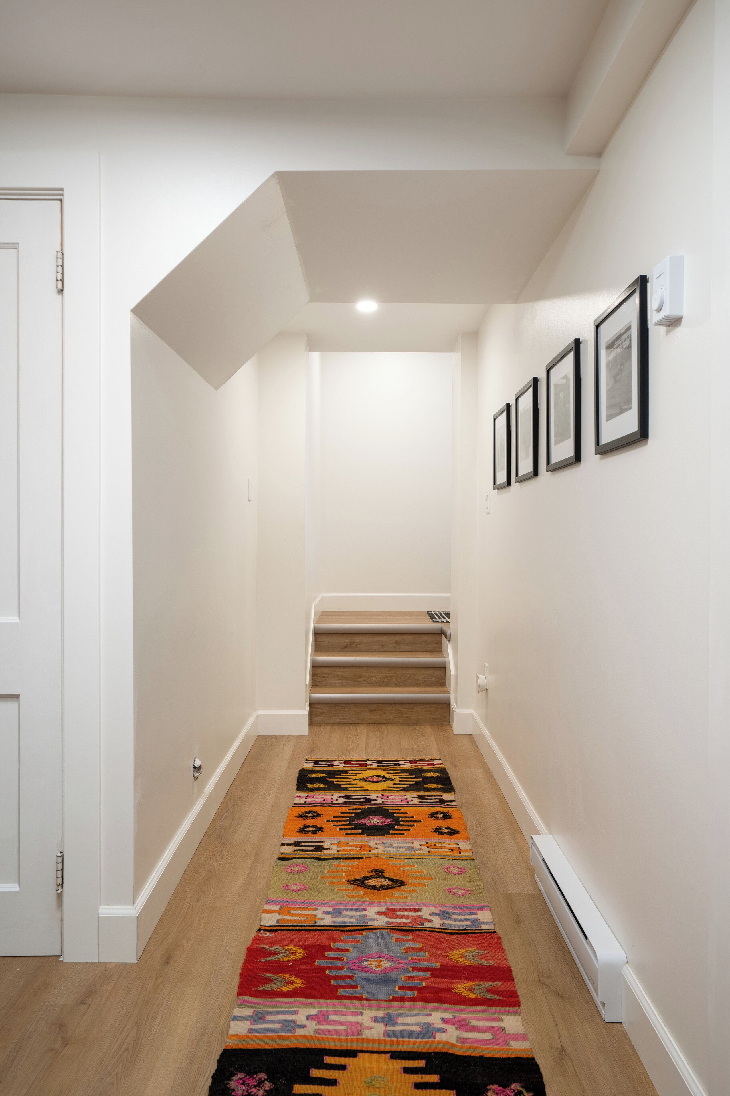 Un couloir doté d’un plancher en bois, de murs blancs et d’un tapis aux couleurs vives.