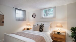 Une chambre à coucher bien rangée, avec un lit, des tables de chevet, des lampes et une fenêtre.