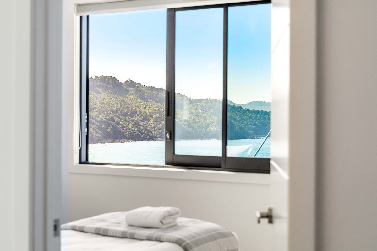 A bedroom with a large window overlooking a coastal landscape.