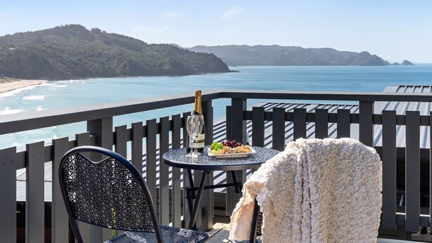 Un balcón con vistas a la playa, una mesa con una botella y aperitivos, y una silla.