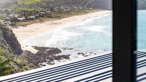 Vista costera desde el interior de un edificio, con vista a una playa de aguas cristalinas y un paisaje montañoso en la distancia.
