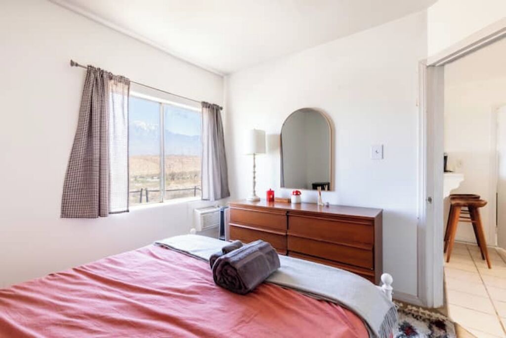 A bedroom with a bed, a dresser, a mirror, and a window with curtains.