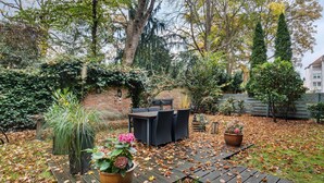 A patio with a table and chairs, surrounded by potted plants and a brick wall. - Apartment 'Hannover Südstadt-Perle' with Private Garden and Wi-Fi (Hannover)