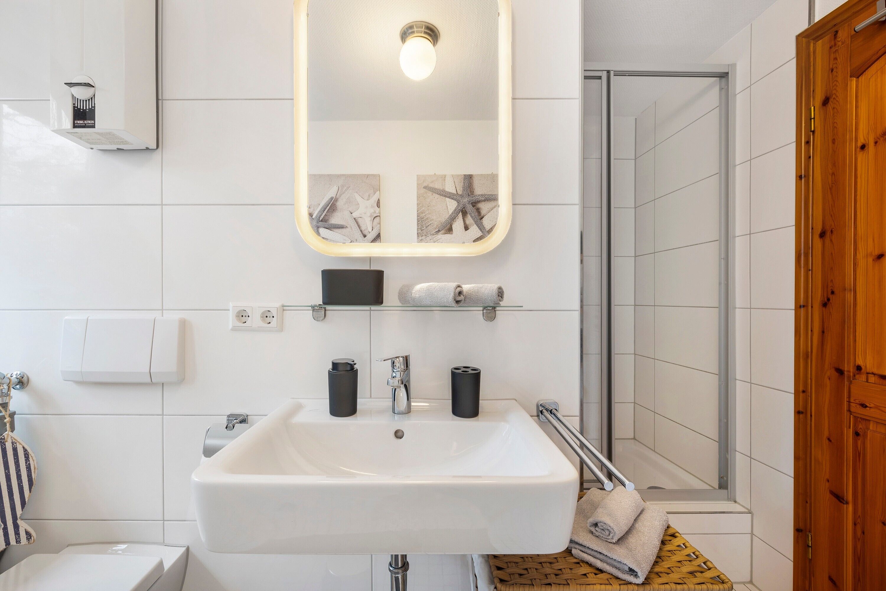 A bathroom with a white sink, a mirror, a towel dispenser, and a shower area.