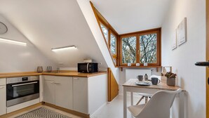 A modern kitchen with a built-in oven, a microwave, and a dining area with a table and chairs. - Apartment 'Hannover Südstadt-Perle' with Private Garden and Wi-Fi (Hannover)