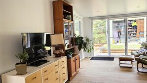 Un salon spacieux doté d’un téléviseur à écran plat, d’un meuble en bois et d’une grande porte-fenêtre coulissante donnant sur un jardin.