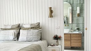 Une chambre à coucher avec un lit, une table de chevet et une salle de bain visible à travers une porte ouverte.
