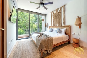 A bedroom with a bed, a ceiling fan, a large window, and a macrame wall hanging.