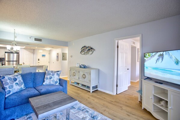 A living room with a blue sofa, a wooden coffee table, and a television displaying a beach scene.