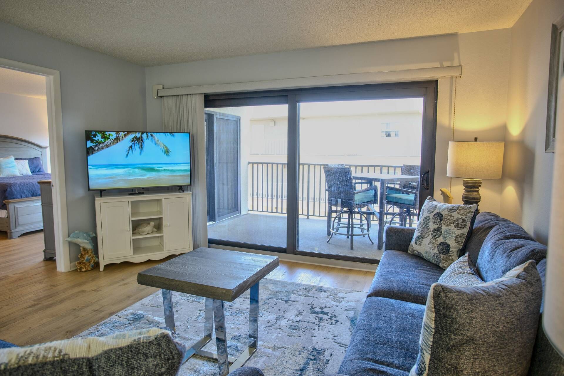 A living room with a sofa, a coffee table, a TV, and a balcony with outdoor furniture.