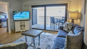 Een woonkamer met een bank, een salontafel, een televisie en een balkon met tuinmeubilair.