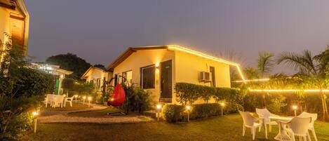 Una casa con exterior iluminado, una hamaca roja colgante y mobiliario exterior.
