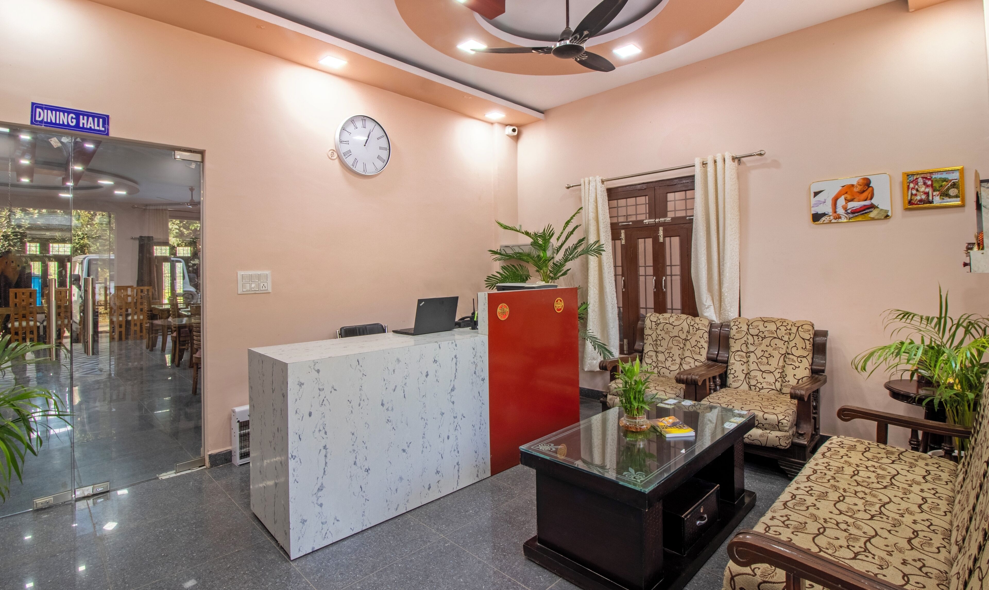 Un espace d’accueil avec une horloge, un panneau indiquant l’emplacement de la salle à manger, un comptoir d’accueil, des sièges et un ventilateur de plafond.