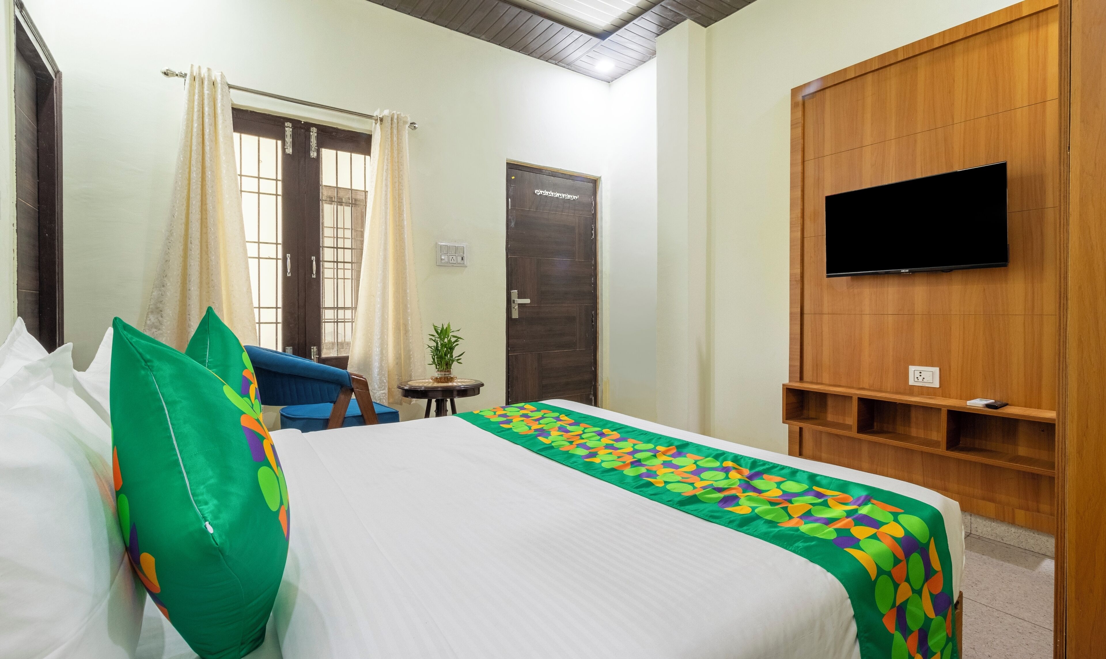 A hotel room with a bed, a TV mounted on the wall, a small table, and a chair.