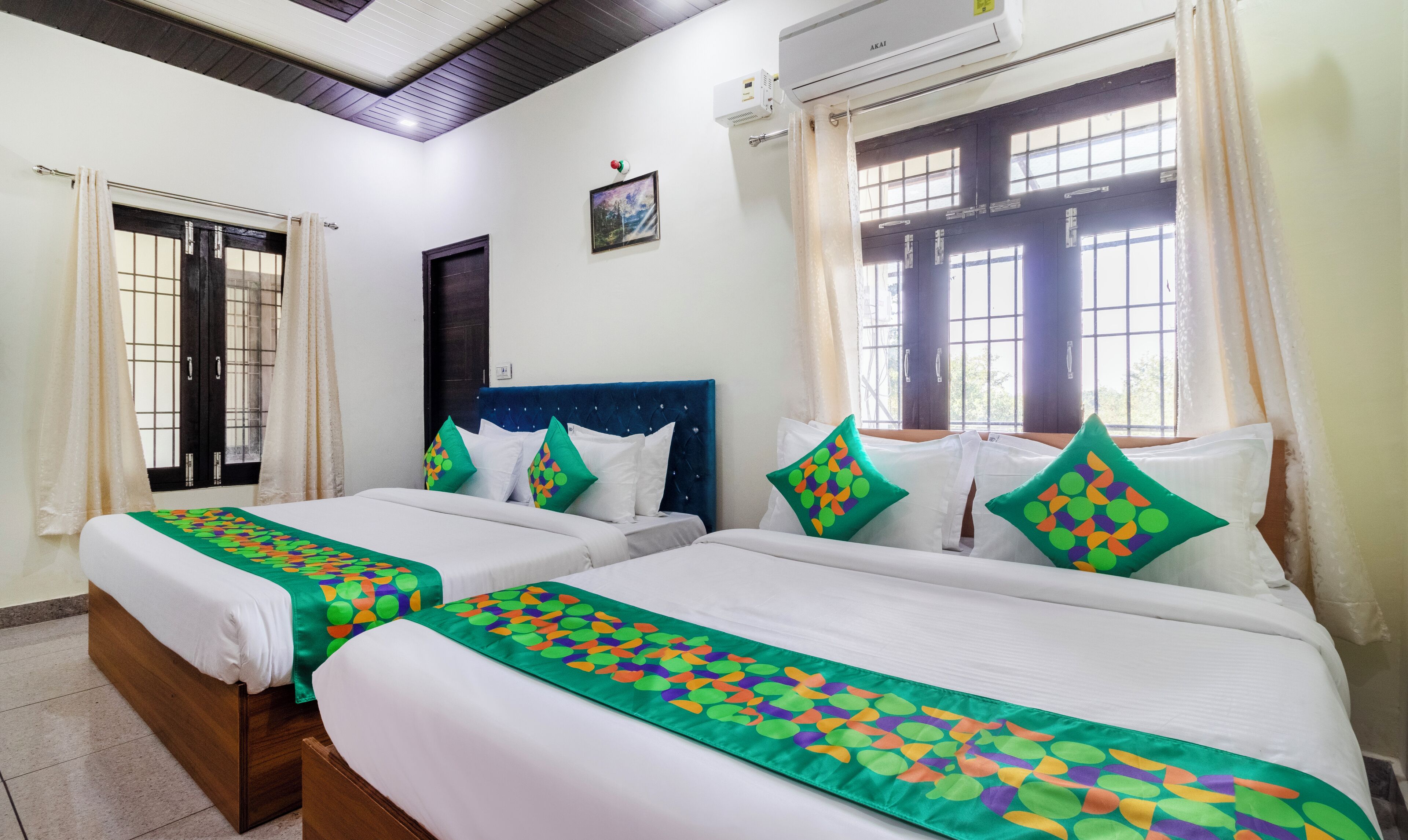 A hotel room with two beds, each with a green and white patterned bedspread, a dark blue headboard, and white pillows.