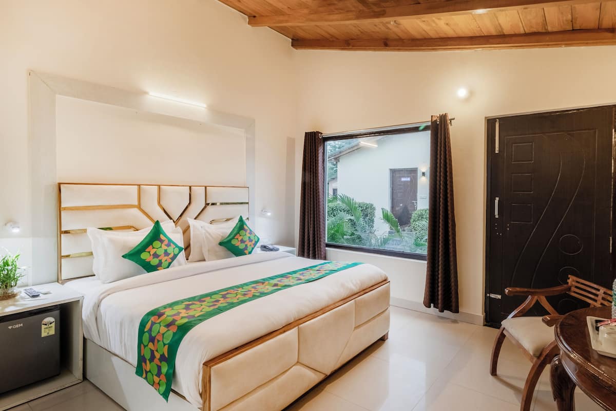 Habitación de hotel con cama, mesita de noche, lámpara y vistas al exterior.