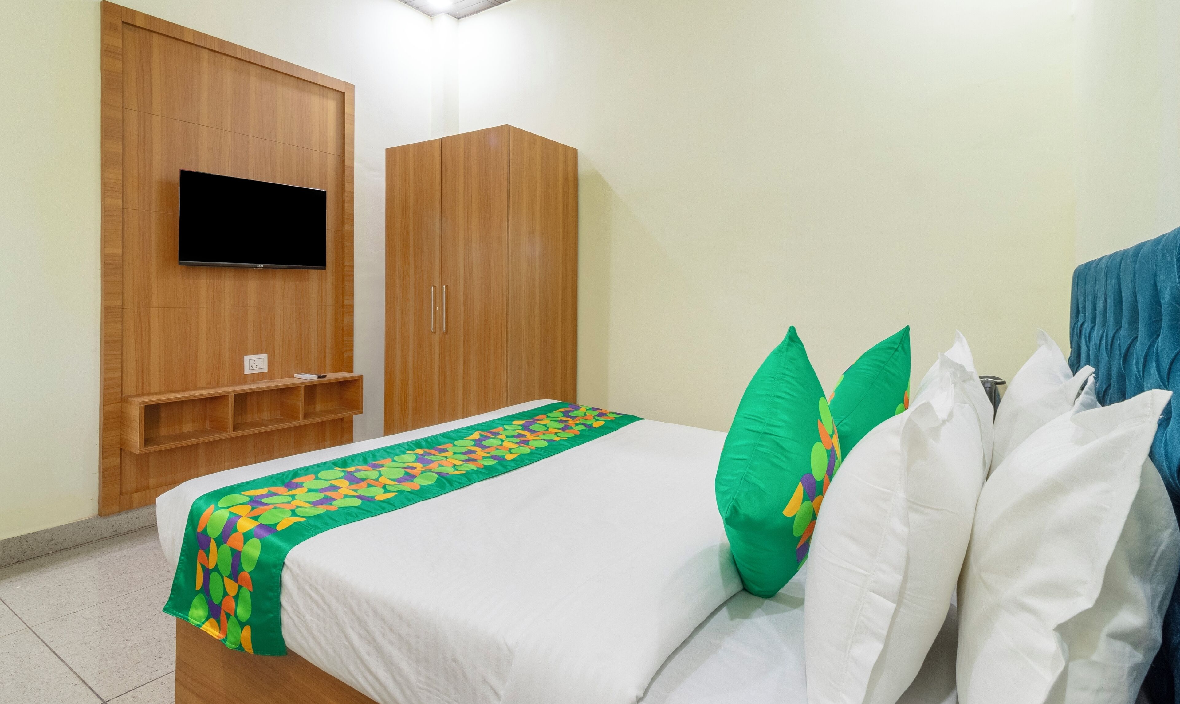 A hotel room with a bed, a TV mounted on a wooden panel, and a wardrobe.