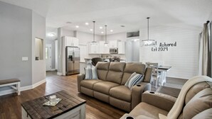 A spacious living room with a sofa and armchair, a wooden coffee table, and a kitchen in the background. - Waterfront 3BR Home | Private Boat Ramp & Firepit | 2 Small Dogs Welcome (Middleburg)