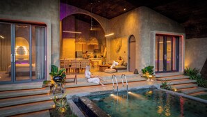 Een modern buitenzwembad met een overdekte spa, een eethoek en een keuken zichtbaar door een boog.