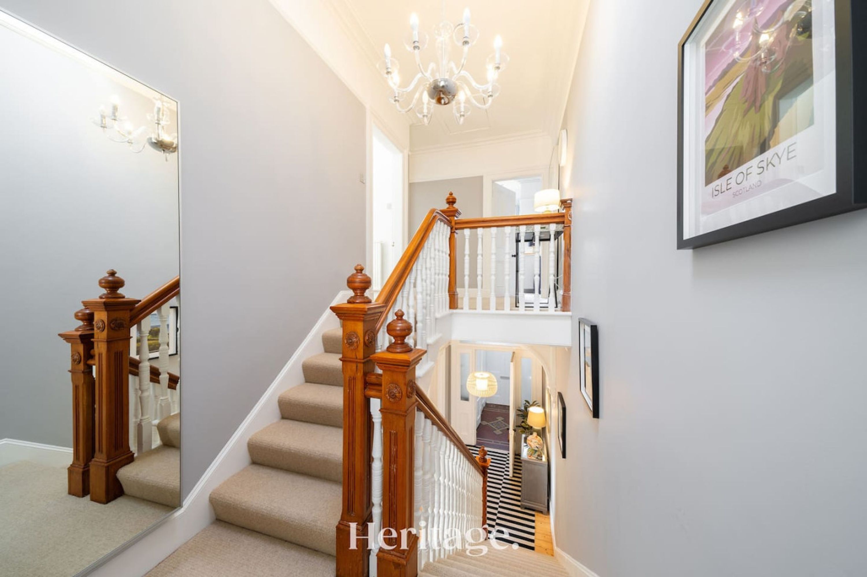 A staircase with wooden balusters and a chandelier, leading to a landing with a framed picture.