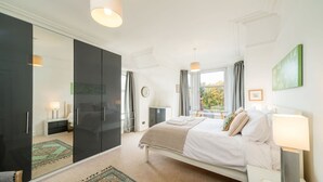 A bedroom with a bed, bedside tables, a wardrobe, a window with curtains, and a view of trees outside. - Sunnybrae House Seaside Family-friendly Getaway in Stonehaven With Hot Tub (Stonehaven)