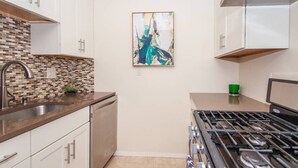 A modern kitchen with white cabinets, a tiled backsplash, a gas stove, and a sink. - Sleek Boston Condo | near South End (Boston)
