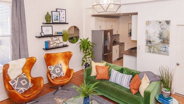 A modern living room with a green sofa, two brown armchairs, a glass coffee table, and a kitchen in the background. - Sleek Boston Condo | near South End (Boston)