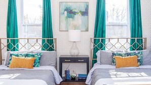 A bedroom with two beds, teal curtains, a painting on the wall, and a bedside table with books. - Sleek Boston Condo | near South End (Boston)