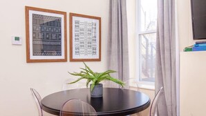 A round dining table with a black top, surrounded by four clear plastic chairs. Two framed artworks are hung on the wall above the table. - Sleek Boston Condo | near South End (Boston)