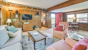 Una sala de estar acogedora con paneles de madera, un televisor, un sofá, una silla y una mesa de comedor.