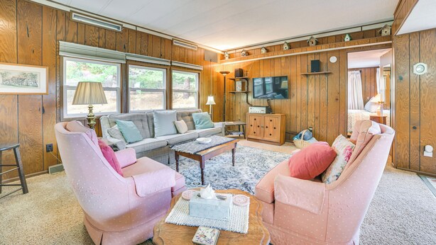 Un salón acogedor con un sofá, dos sillones rosados, una mesa de centro y una televisión.