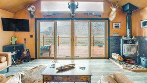 A spacious living room with a large wooden ceiling, a mounted bull head, a fireplace, and a view of the mountains through large glass doors. - Colorado River Getaway in Parachute: Dogs Welcome! (Parachute)