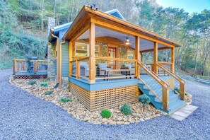 Una cabaña con terraza de madera, paredes de piedra y un porche cubierto con mobiliario exterior.