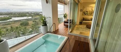 A balcony with a swimming pool, a glass door leading to a living area, and a view of a river and cityscape.