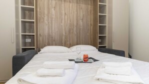 A neatly made bed with white linens and towels, a glass of water, and a red glass on a tray.