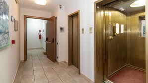 A hotel corridor with a door leading to an elevator, a fire extinguisher, and a ceiling light fixture.