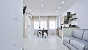 Una cucina moderna con mobili bianchi, un'area pranzo con tavolo e sedie, e un divano grigio.