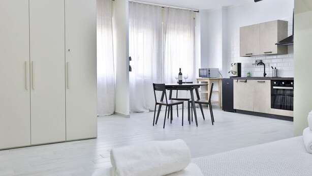 Una camera d'albergo moderna con un letto, una scrivania, una sedia, un tavolo da pranzo e un angolo cottura.