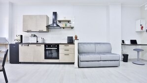 Una cucina moderna con mobili chiari in legno, una cappa aspirante nera e un divano grigio.