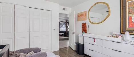 Une chambre à coucher comprenant un lit, une commode, un miroir et une porte donnant sur une autre pièce.