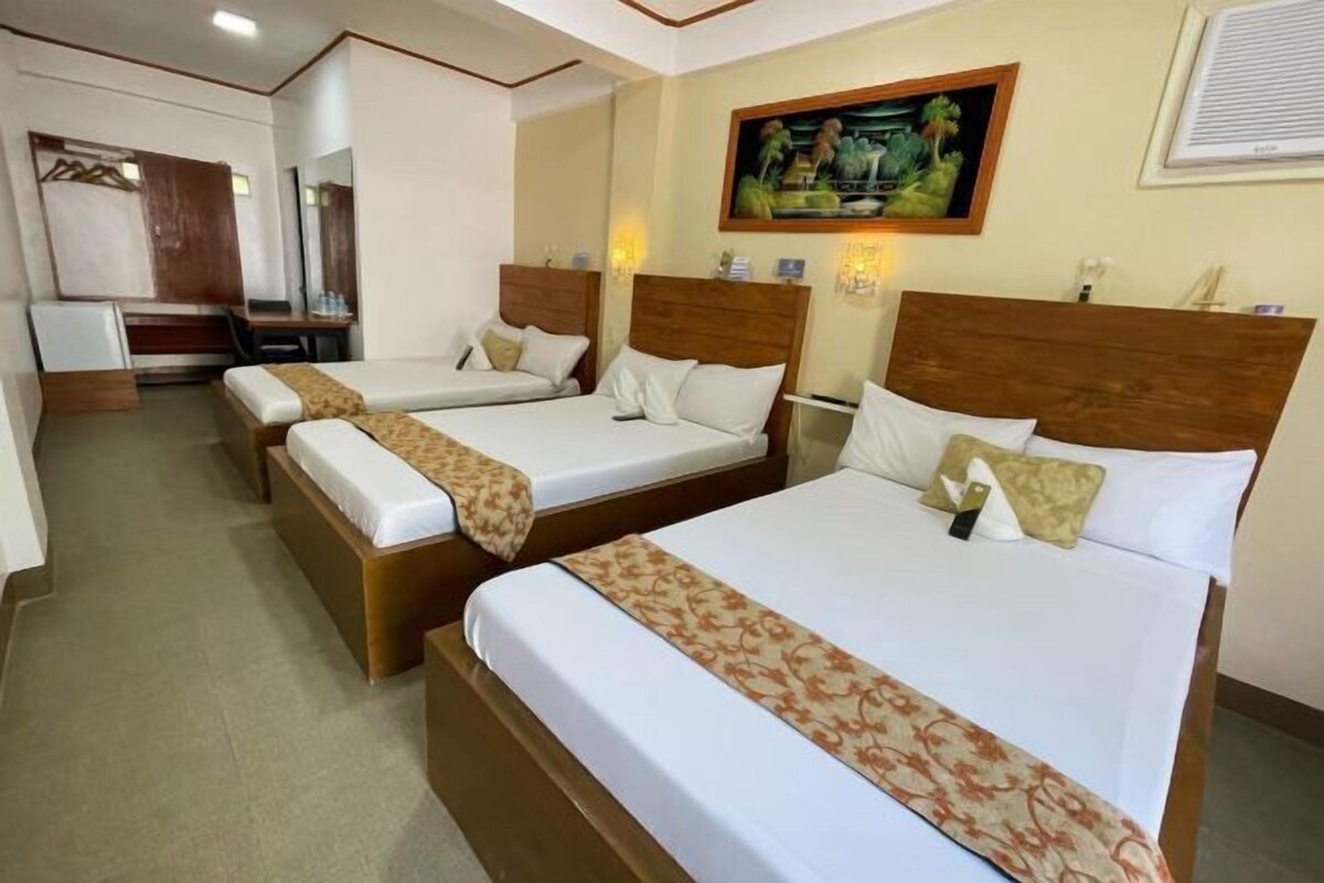A hotel room with three single beds, a desk, and a chair.