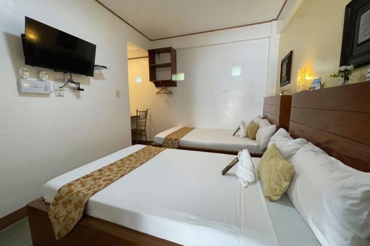 A hotel room with two beds, a flat-screen TV mounted on the wall, a small shelf, and a bedside table with a lamp.