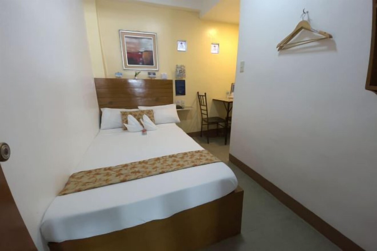 A hotel room with a large bed, a wooden headboard, a desk, and a chair.